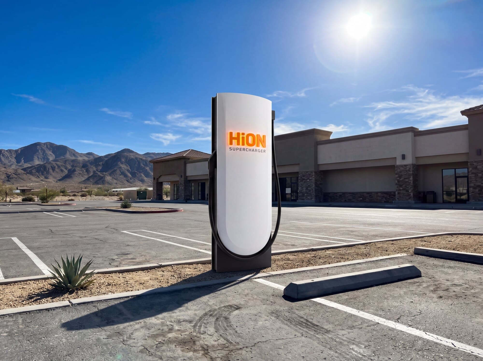 A HiON pillar at a sunlit desert roadside stop, a low retail building and open parking behind it, the matte-white face marked with the glowing orange HiON wordmark.
